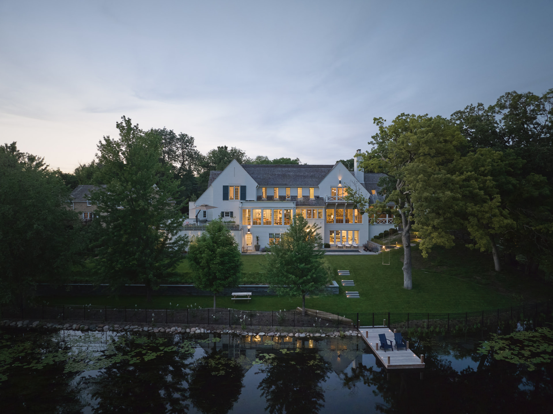 Waters Edge residence illuminated beyond the pond at dusk