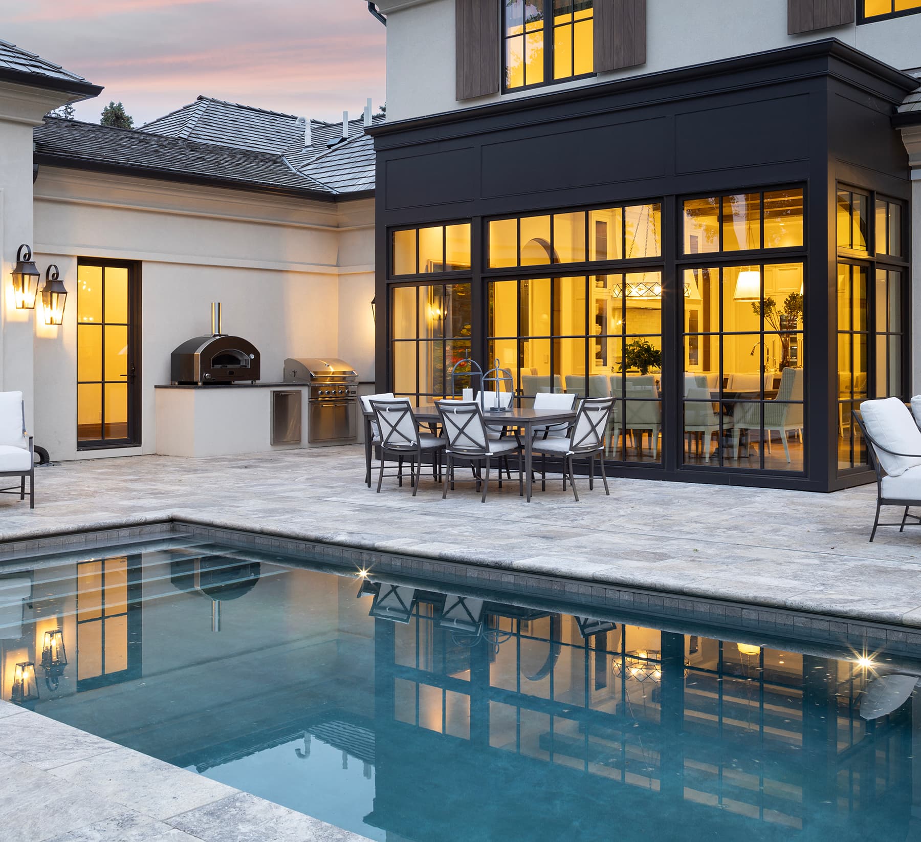 Highcroft courtyard terrace with pizza oven, grill and dining table at dusk
