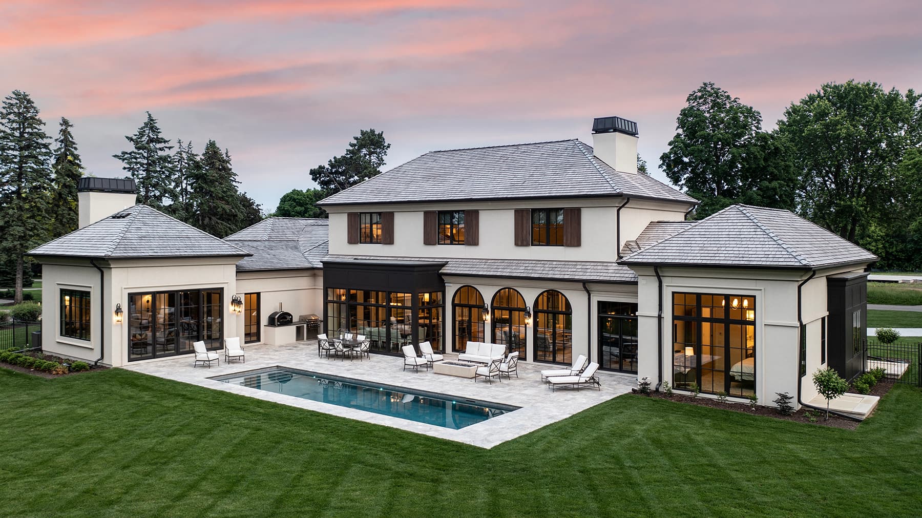 Elevated view of Highcroft's rear terrace, pool and lawn at dusk