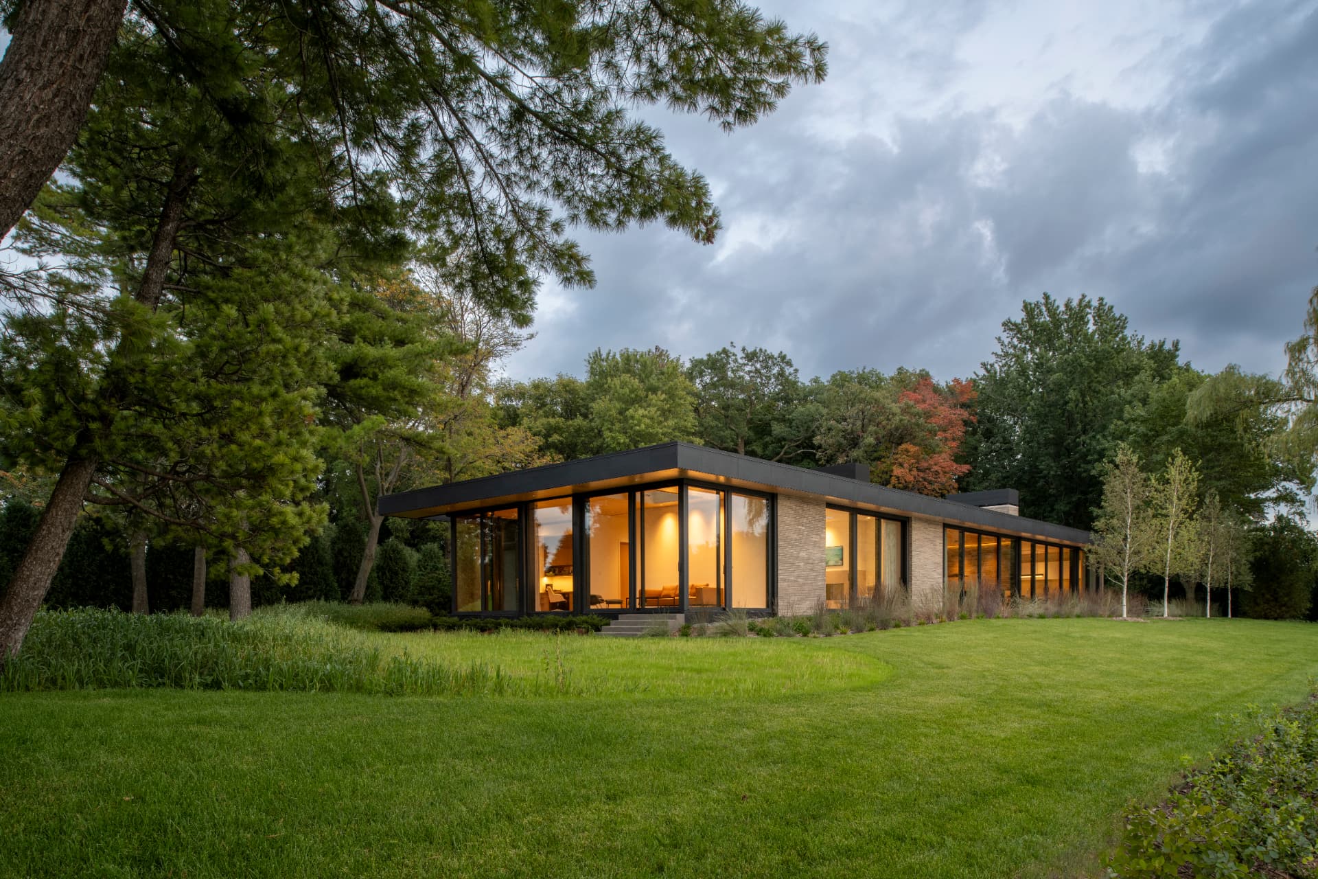 An modern, glass-walled home with a flat cantilevered roof overlooks a lake.