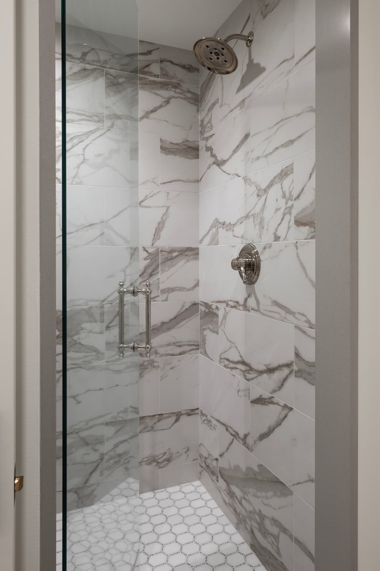 Highcroft shower clad in book-matched marble tile with hexagon mosaic floor