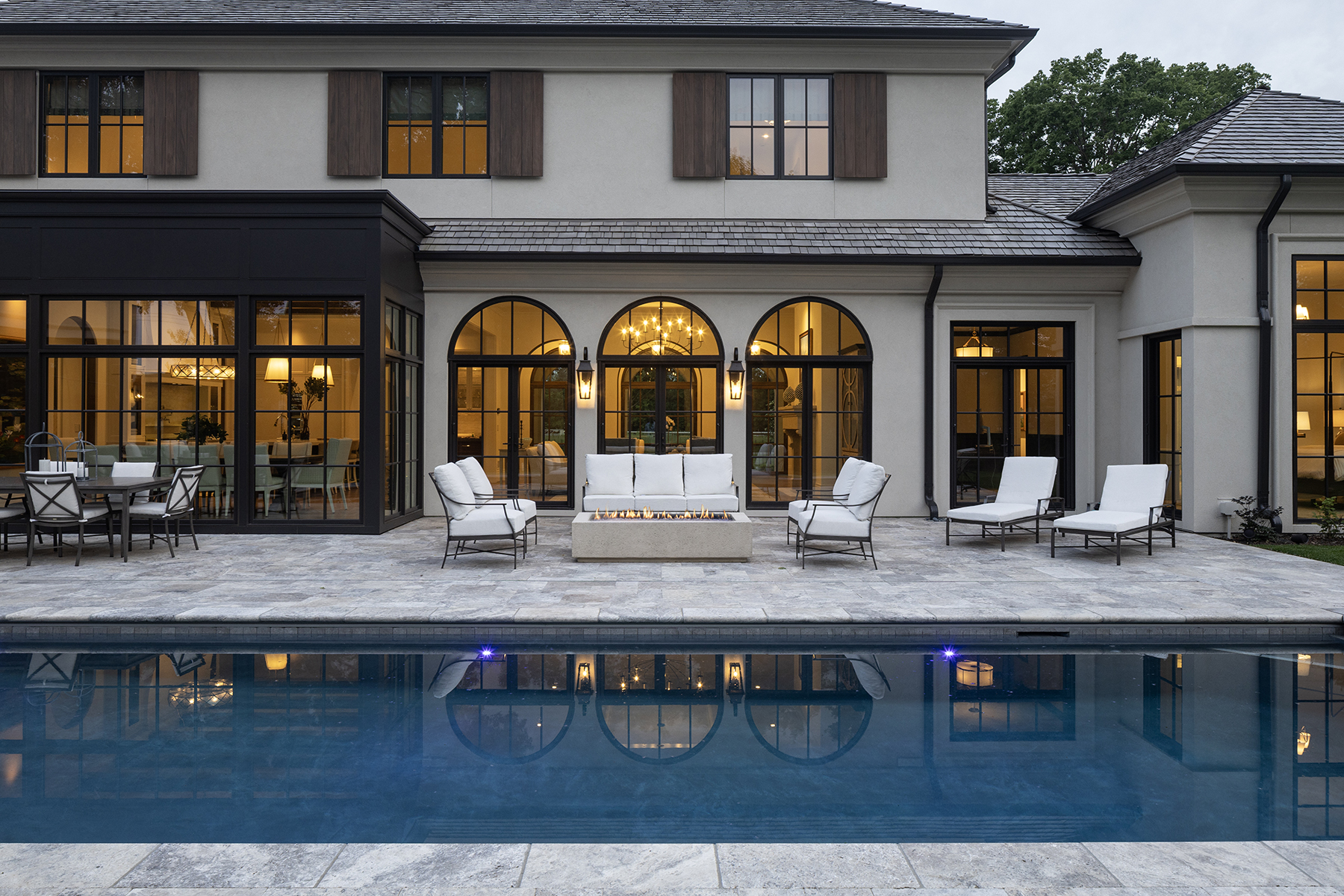 Highcroft pool terrace at dusk with linear fire table and lit arcade